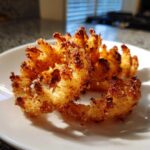 Close-up of two golden brown Air Fryer Crispy Mini Blooming Onions resting on a white plate.