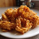 A plate piled high with golden brown Air Fryer Crispy Mini Blooming Onions, perfectly cooked and ready to eat.