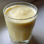 Close-up of a tall glass filled with a creamy, pale yellow Banana Chamomile Tea Smoothie, showing a slight foam on top.