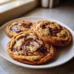 Three freshly baked Brown Butter Chocolate Chip Cookies with melted chocolate chunks on a white plate.