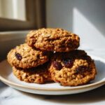 A stack of four chewy Brown Butter Oatmeal Raisin Cookies loaded with oats and plump raisins, resting on a small plate.