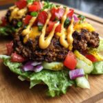 Close-up of a Burger Bowls 30 Minute Dinner Idea featuring a seasoned patty on lettuce with cheese, pickles, tomatoes, and a drizzle of sauce.