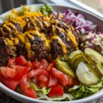 Close-up of a fully assembled Burger Bowls 30 Minute Dinner Idea with seasoned ground beef, melted cheese, lettuce, tomatoes, pickles, and sauce.