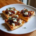 Three savory Caramelized Onion and Goat Cheese Tarts appetizers served on a white plate, topped with fresh thyme.
