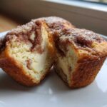 A close-up of Cheesecake Muffins with Cinnamon cut in half, showing the creamy cheesecake filling inside the cinnamon-swirled cake.