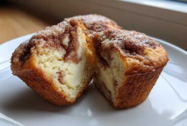 A close-up of Cheesecake Muffins with Cinnamon cut in half, showing the creamy cheesecake filling inside the cinnamon-swirled cake.