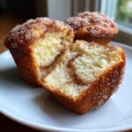 A close-up of a Cheesecake Muffin with Cinnamon, cut in half showing the swirl interior and sugary top.