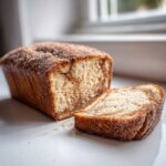 A freshly baked Cinnamon Sugar Donut Bread loaf with one slice cut and resting beside it, coated in sparkling sugar.