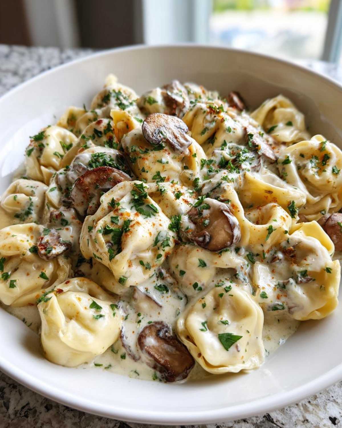 Close-up of a white bowl filled with Creamy Mushroom Tortellini Alfredo, garnished with parsley.
