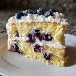 A close-up slice of Fluffy Lemon Blueberry Naked Cake with layers of yellow sponge, whipped cream frosting, and fresh blueberries.