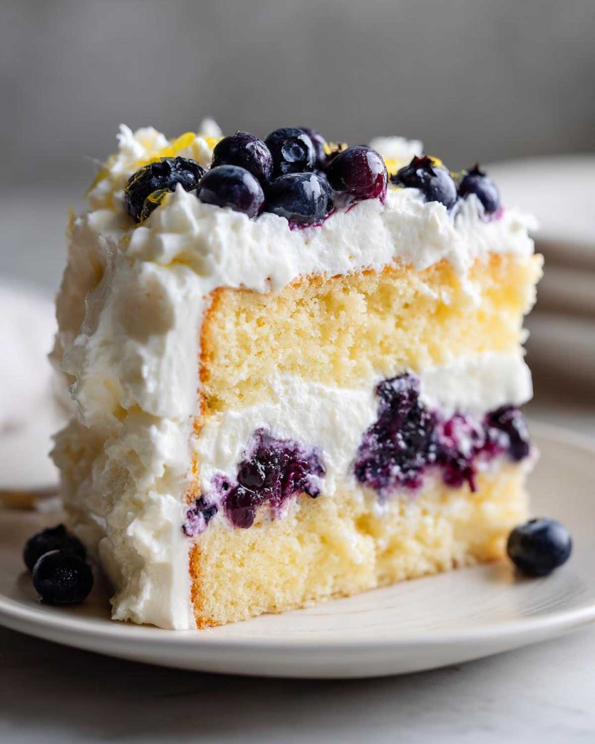 A generous slice of Fluffy Lemon Blueberry Naked Cake Homemade with Whipped Cream Frosting, topped with fresh blueberries.