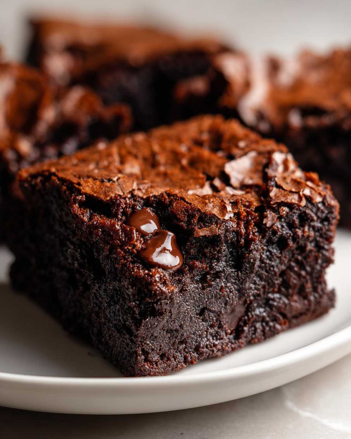 A close-up of a rich, fudgy square of 250 calorie brownies topped with melted chocolate chips on a white plate.
