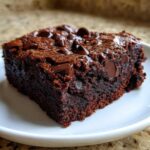 A close-up of a single, rich, fudgy brownie with melted chocolate chips on top.