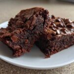 Two fudgy Brownies with Chocolate Chips stacked slightly, showing the dense interior and shiny top.