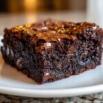 A close-up shot of a single, rich, fudgy square of chocolate chip brownies with a shiny, crackly top.