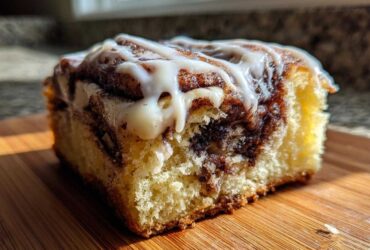 Close-up of a single, gooey square of Cinnamon Roll Bliss Bars with white icing drizzled on top.