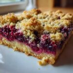 A single serving of vibrant, layered lemon berry dessert squares featuring a thick fruit filling and golden crumb topping.
