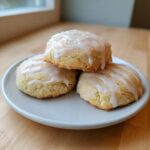 Three soft Lemon Ricotta Cookies stacked on a light blue plate, drizzled with white glaze and coarse sugar.