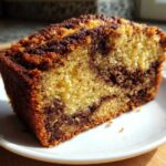Close-up of a moist slice of marbled Apple Cinnamon Bread showing swirls of light and dark batter on a white plate.