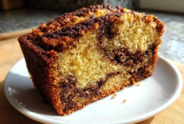 Close-up of a moist slice of marbled Apple Cinnamon Bread showing swirls of light and dark batter on a white plate.