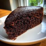 Close-up of a rich, dark slice of Gluten Free Chocolate Cake with a glossy top.
