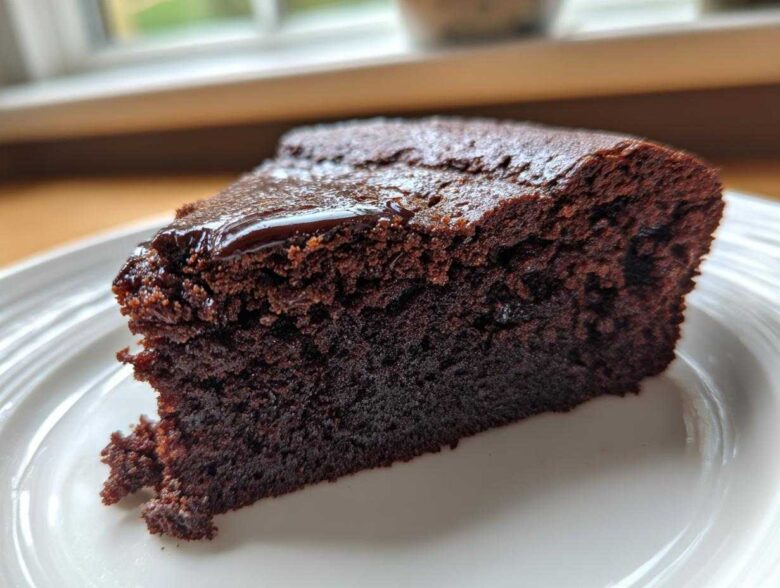 Close-up of a moist slice of Gluten Free Chocolate Cake with a thin, shiny chocolate glaze on top, served on a white plate.