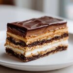 A perfect rectangular slice of Peanut Butter Chocolate Lasagna showing distinct layers of chocolate crust, cream, peanut butter, and glossy chocolate topping.