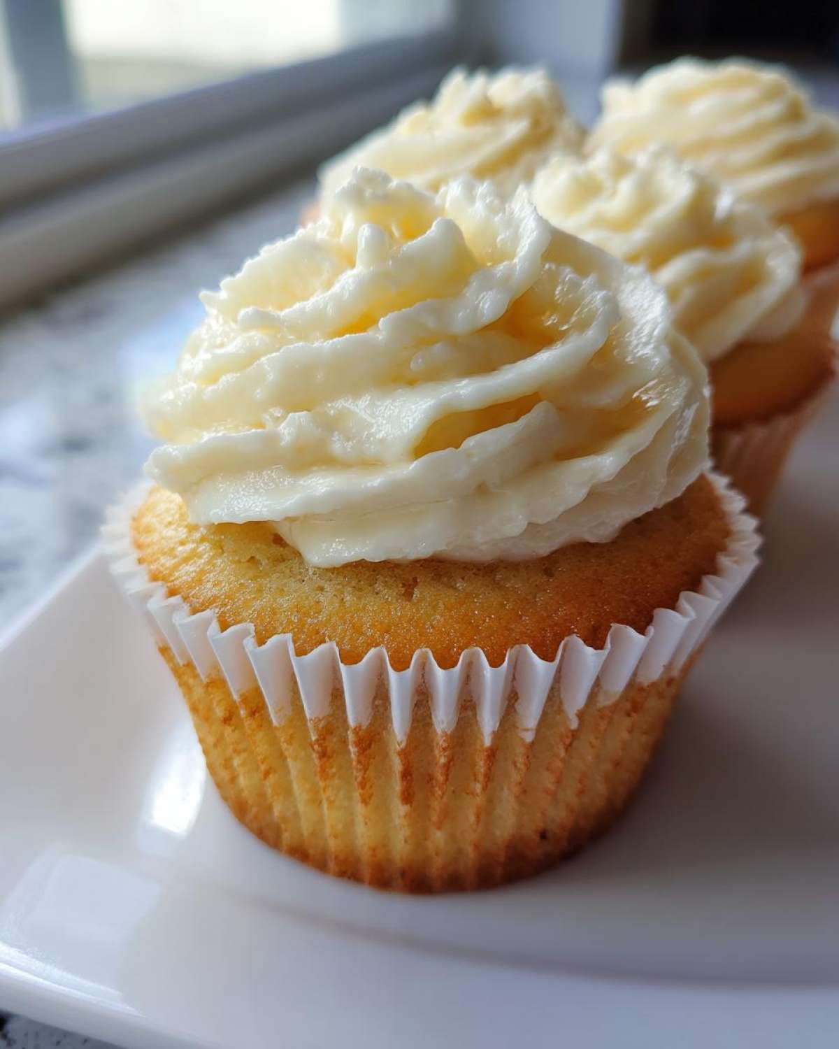 Close-up of a perfectly baked vanilla cupcake topped with thick, swirled white frosting.