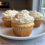 Four vanilla cupcakes topped with generous swirls of white buttercream frosting, ready to eat.