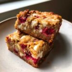 Two decadent Raspberry White Chocolate Blondies stacked on a speckled white plate, showing visible white chocolate chunks and bright red raspberries.
