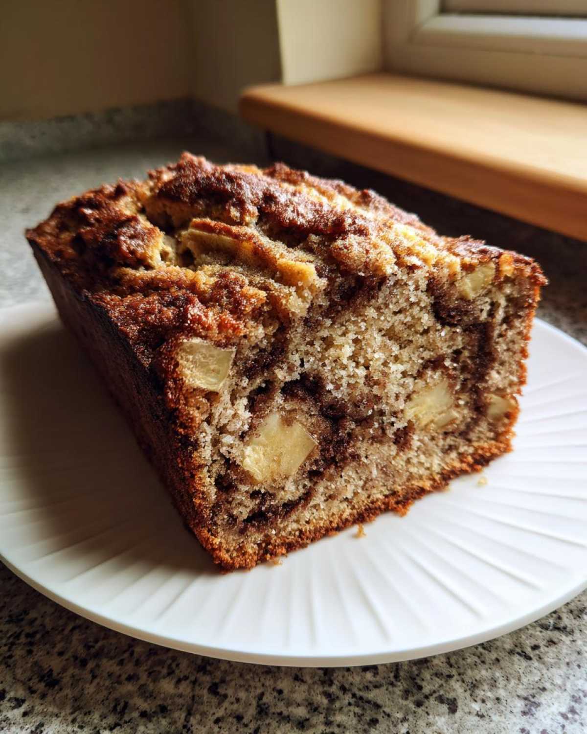 Close-up of a thick slice of Apple Cinnamon Bread showing moist crumb, visible apple chunks, and a dark cinnamon swirl.