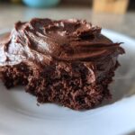 A close-up of a bite taken out of a rich chocolate cake topped with thick Chocolate Buttercream Frosting.