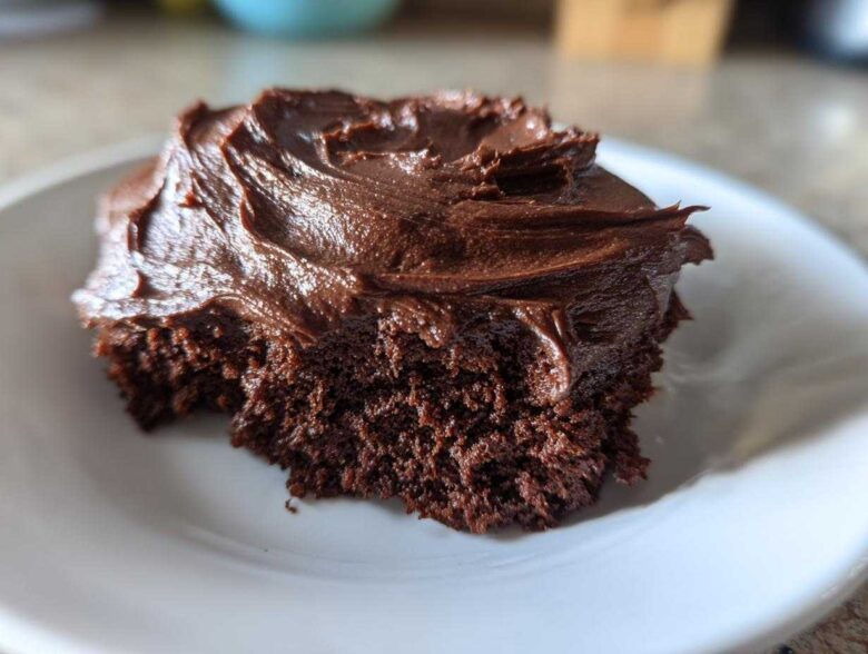 A close-up of a bite taken out of a rich chocolate cake topped with thick Chocolate Buttercream Frosting.